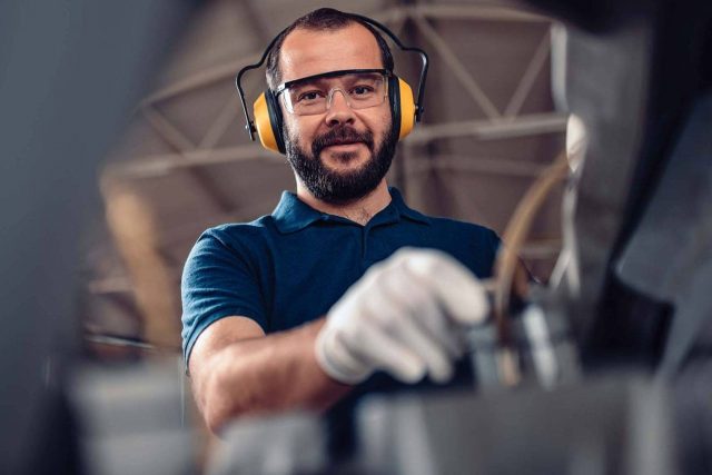 bearded man in protective safety earmuffs and protective goggles operating a piece of machinery